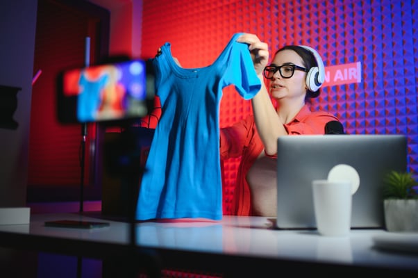 A woman livestreaming, showcasing a blue shirt.