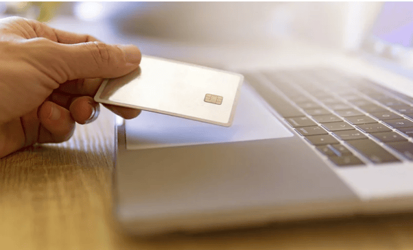 Hand holding credit card near laptop keyboard.